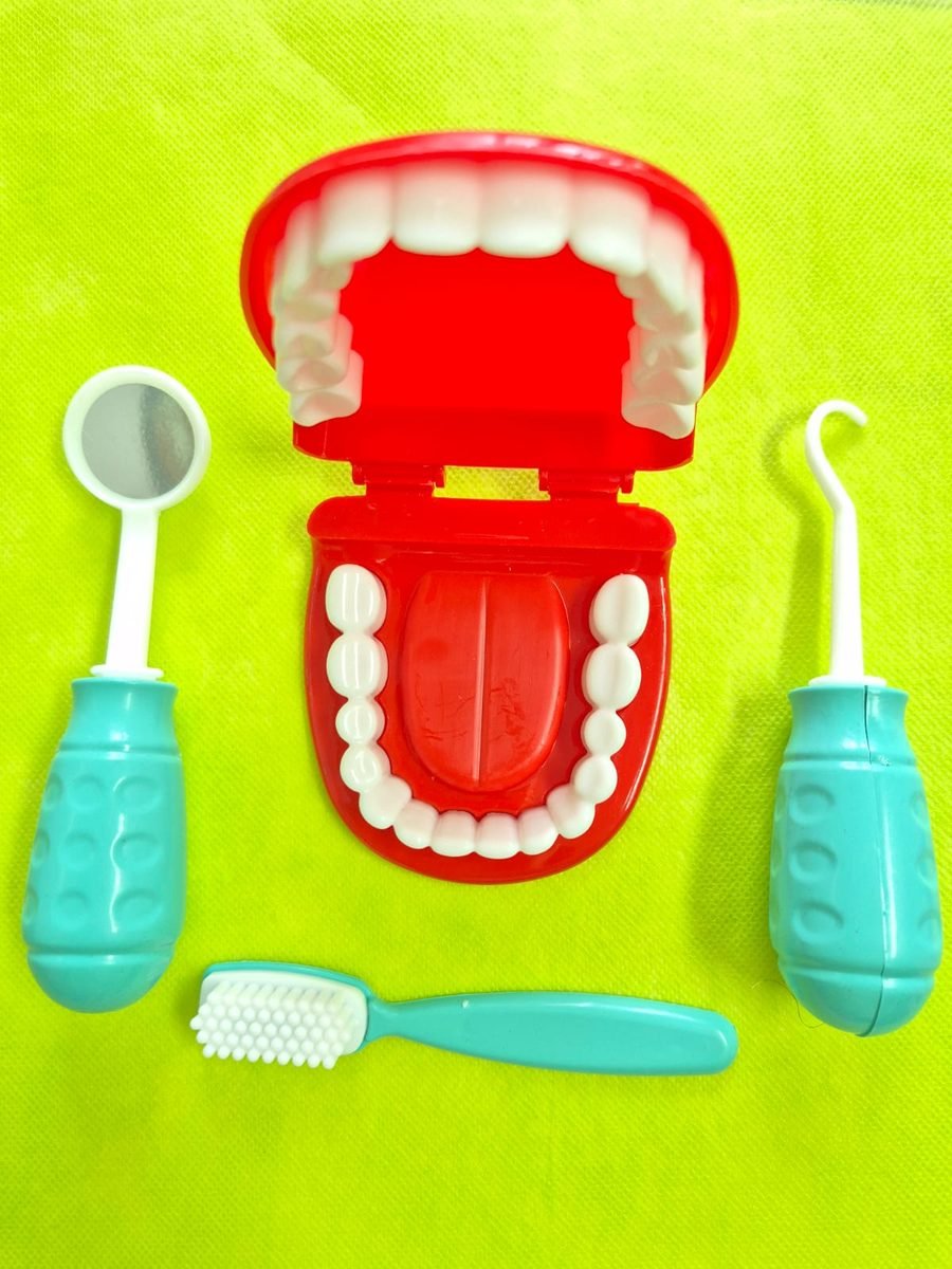 Modelo de arcada dentária vermelha aberta, com espelho, sonda e escova de dente de brinquedo ao redor.
