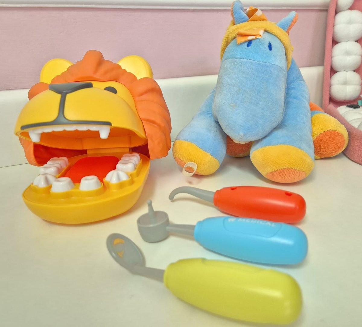Leão de brinquedo com a boca aberta mostrando os dentes, cavalinho de pelúcia e instrumentos coloridos de dentista de brinquedo.
