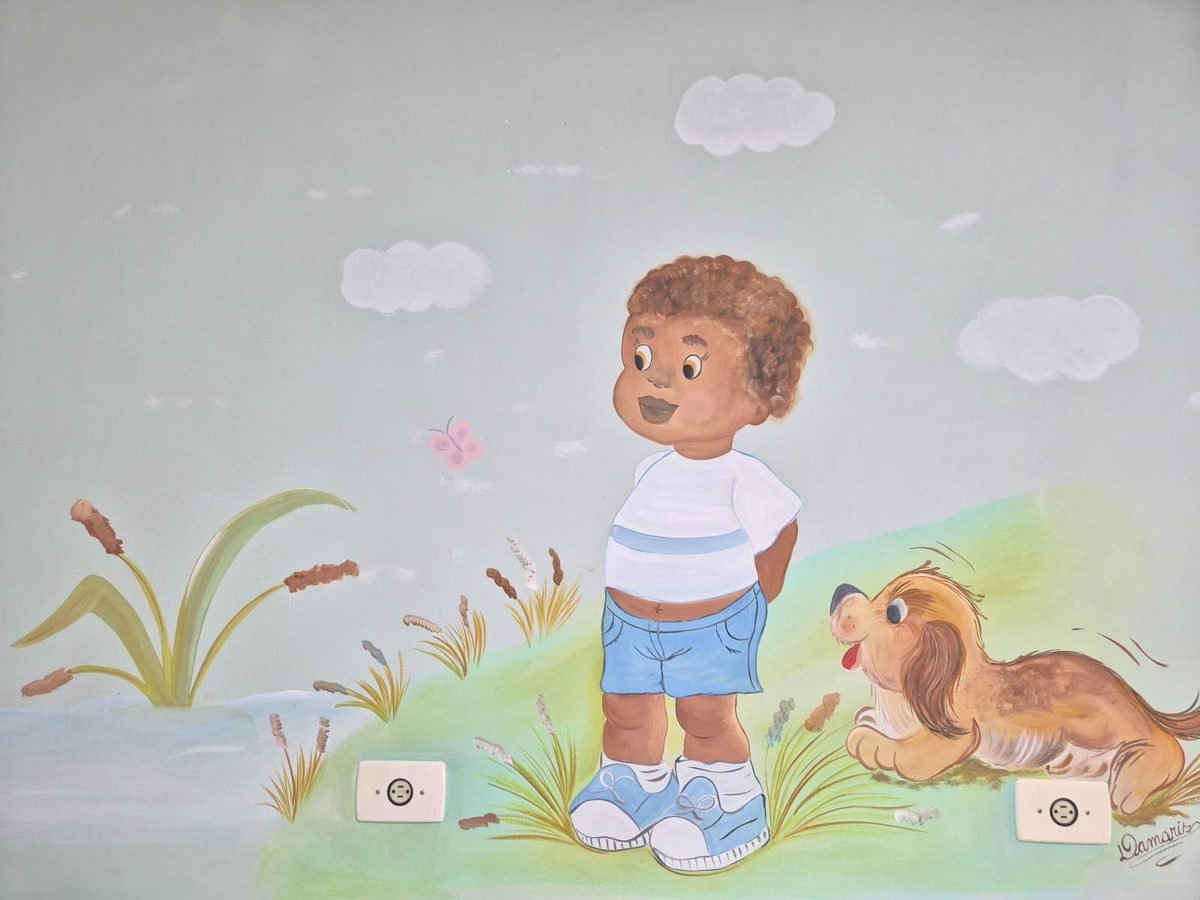 Mural pintado à mão: menino sorridente ao lado de um cachorrinho deitado na grama, com nuvens e borboleta.